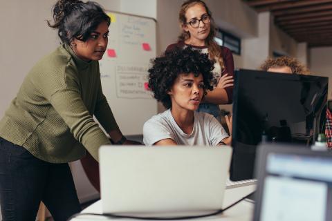 People looking at computer screens, whiteboard in background. 