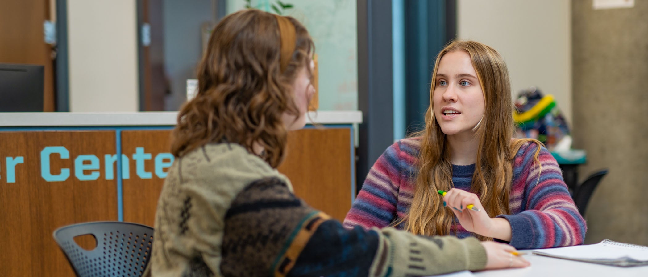 Two students sitting at table talking in front of Career Center front desk